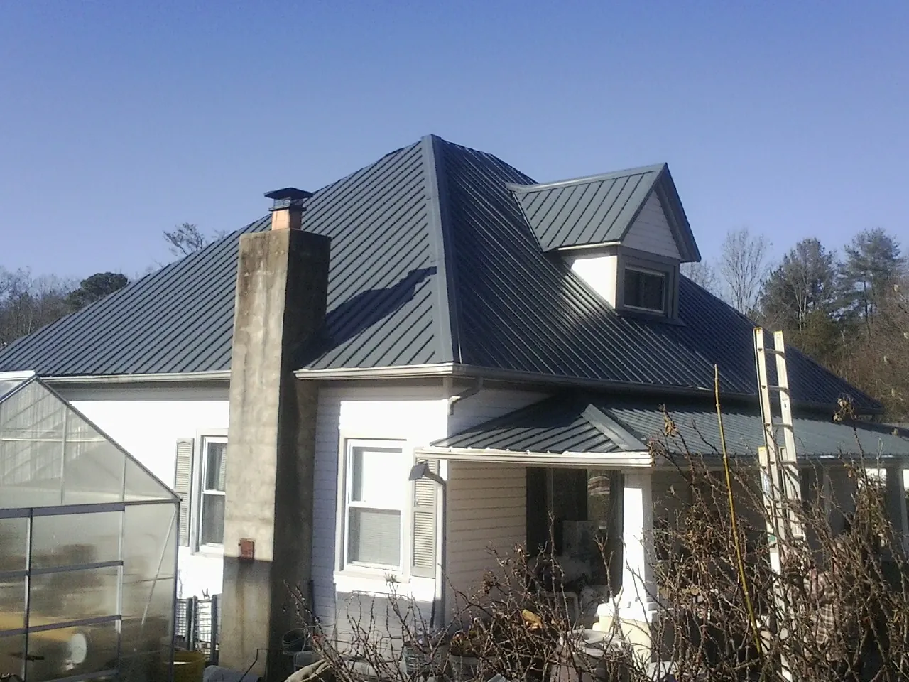 Dark blue standing seam metal roof on a white farmhouse with dormer — Slate & Tile Roof Repair by Roofing Brothers in Madbury