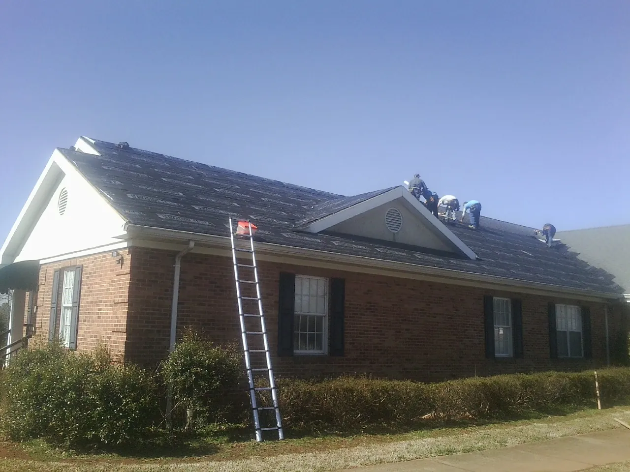 Crew tearing shingles off a brick ranch roof with a ladder set — Emergency Roof Repair work by our crew in Madbury