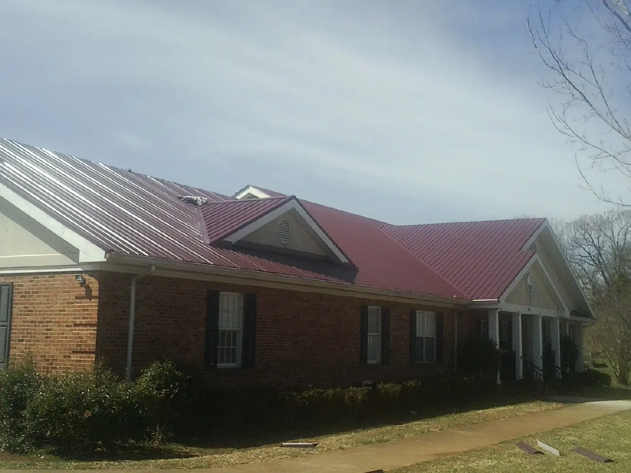 Red metal roof with gabled entries on a long brick building, from a Hail Damage Roof Repair job in Madbury