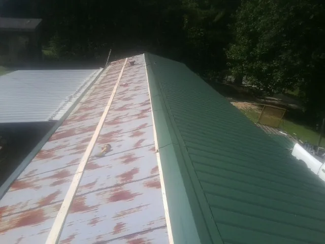 Old rusted panels beside newly installed green metal roofing — Wind Damage Roof Repair by Roofing Brothers in Madbury