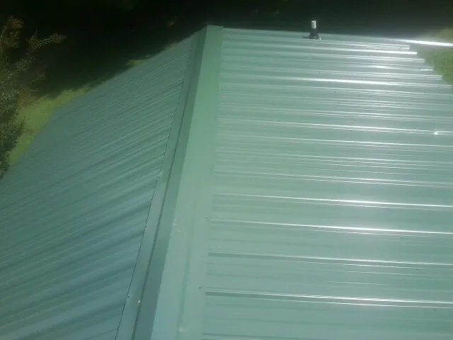 New green metal panels meeting at the ridge of a roof — Flat Roof Repair work by our crew in Madbury