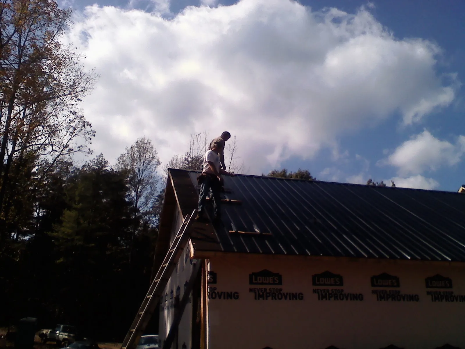 Roofer fastening dark metal panels high against a cloudy sky, from a Roof Inspection job in Madbury