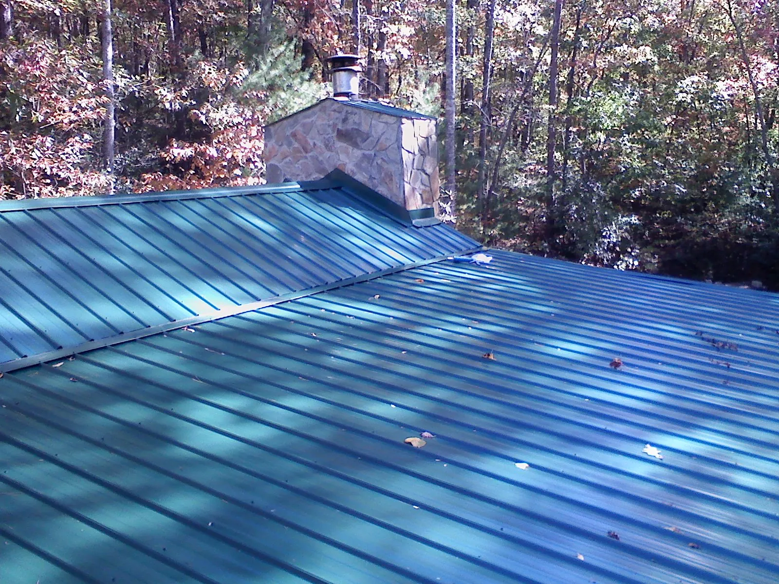 New green metal roof and stone chimney surrounded by autumn woods in Madbury