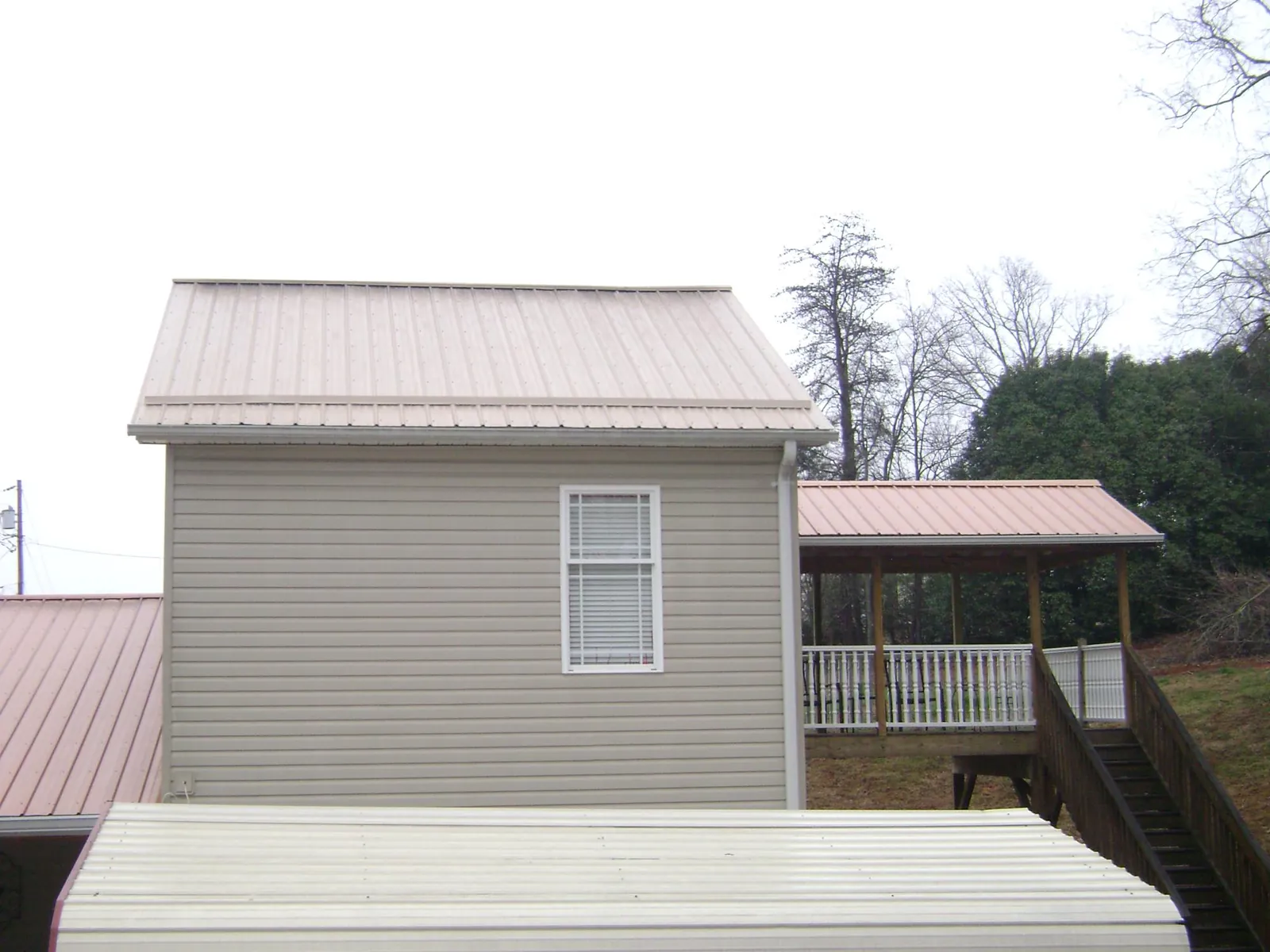 Tan metal roofs on a two story addition and attached porch, from a Roof Replacement job in Madbury
